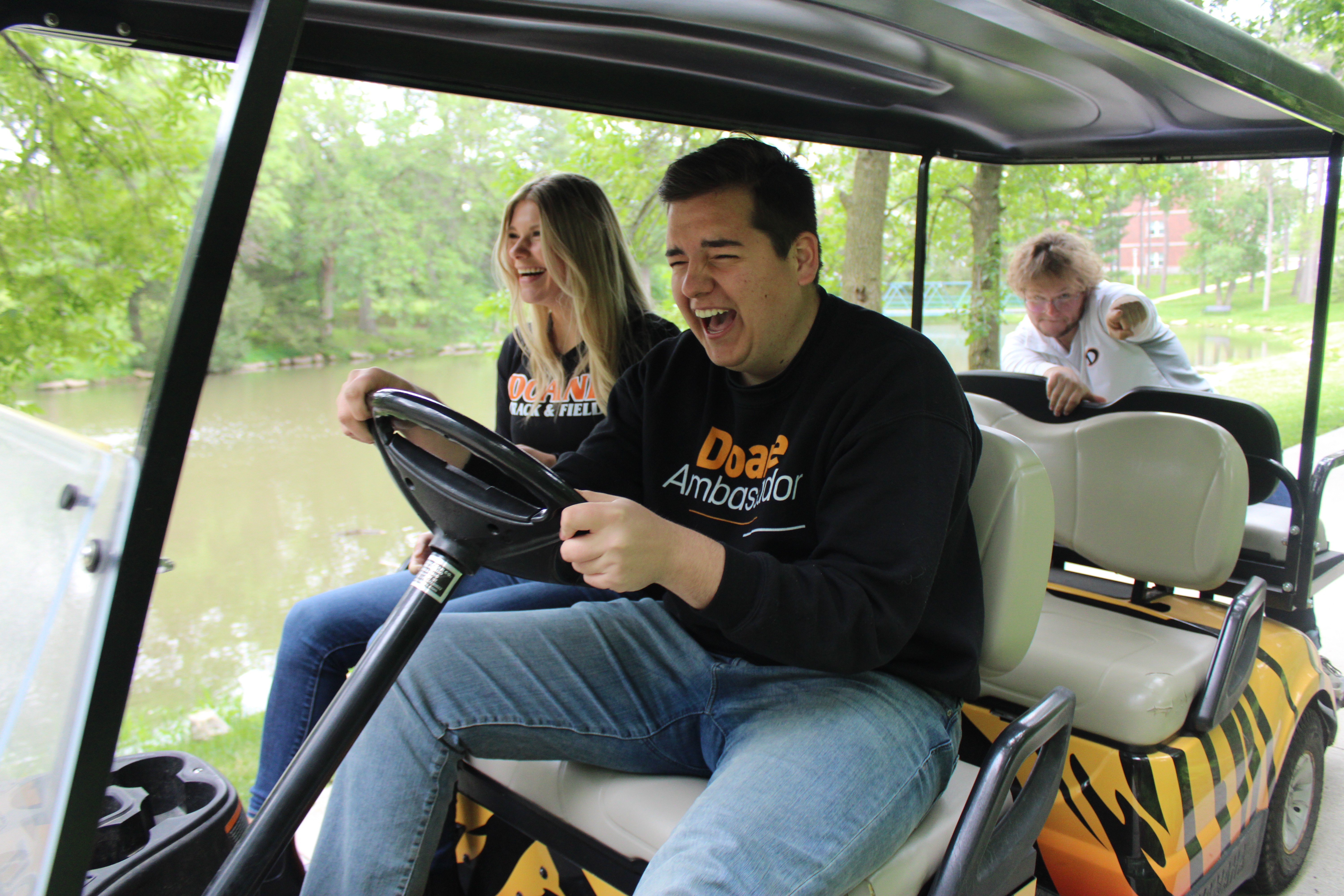 Two Doane alumni driving a golf car, with big smiles.